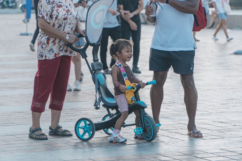 Enfant pédalant seul sur un tricycle sous la surveillance d'un parent