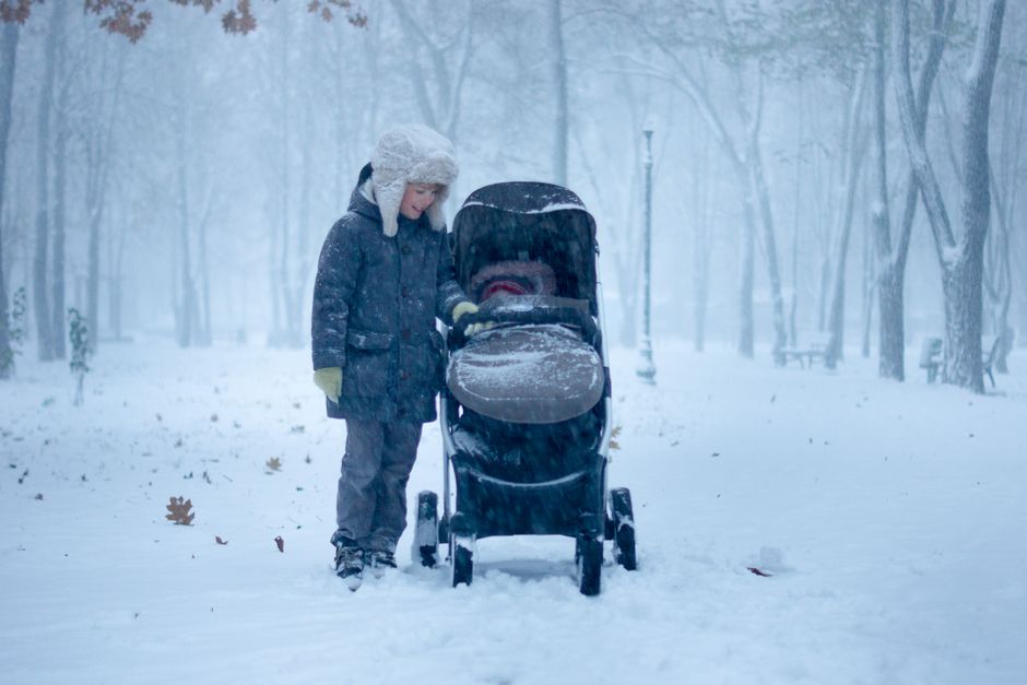 Enfant près d'une poussette dans la neige
